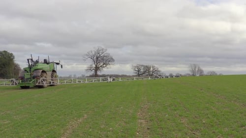 Tractor Spraying Vast Green Field on Overcast Day