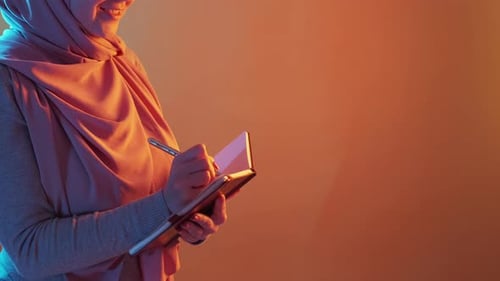 Woman Writes in Notebook with Pink Headscarf