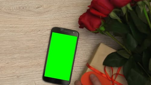 Smartphone with Green Screen Next to Gift and Roses