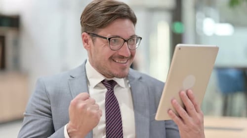 Man Celebrates Success on Tablet in Office