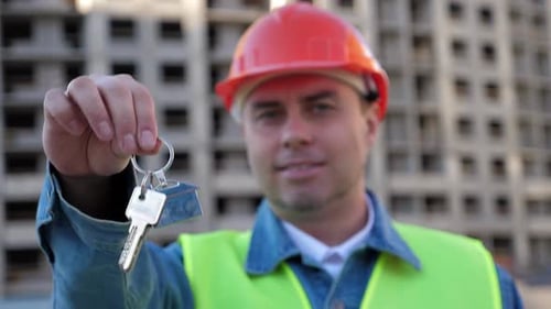 Arbeiteringenieur im gelben Schutzhelm zeigt den Schlüssel auf der Baustelle