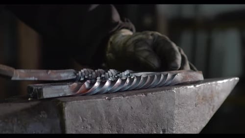 Unrecognizable forger putting metal details on anvil in workshop
