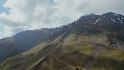 Aerial View of a Mountain Dirt Road Ascending a Pass Covered with Clouds