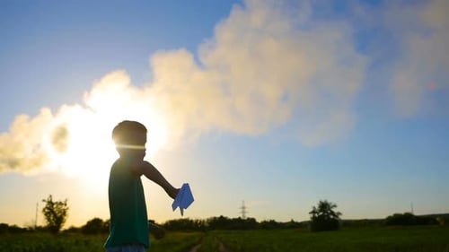 Child Launches Paper Airplane at Sunset in Field