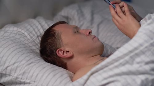 Young Adult Lies in Bed Using Smartphone