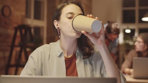 Young Woman Working on Laptop and Drinking Coffee at Office Desk