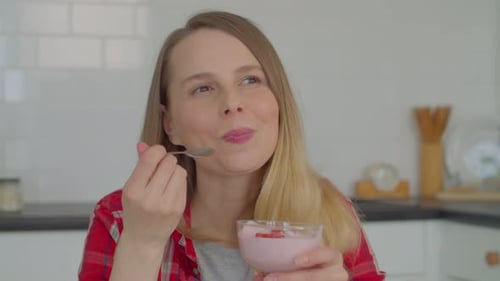 Woman Eats Strawberry Yogurt in Kitchen