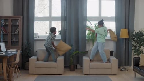 Des frères et sœurs métisses se battent d'oreillers dans le salon