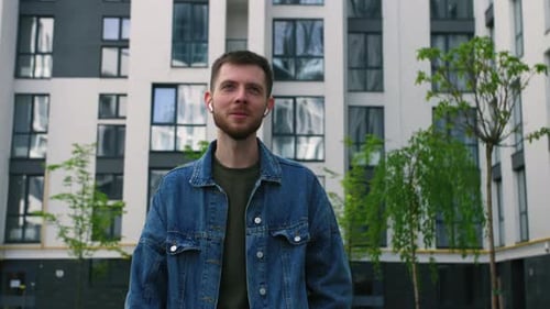 Happy Young Man Listening Music in Wireless Earphones While Walking and Dancing on Street