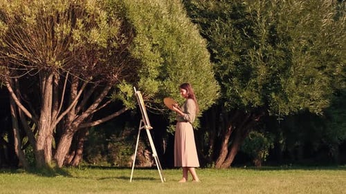 Cheerful Woman Artist Paints a Picture on Canvas While Standing in a Park in Sunny Weather