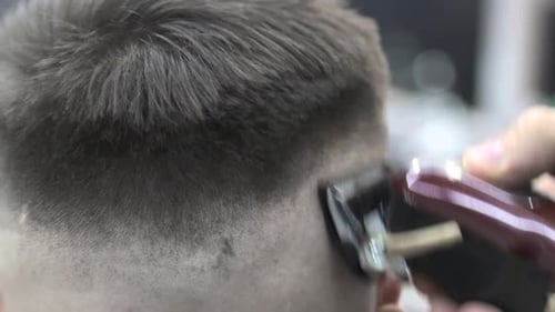 Barber verwendet eine Haarschneidemaschine, um dem Kunden die Haare auf einem Stuhl zu schneiden. Close-Up Clipper rasiert Haare