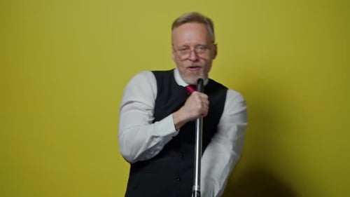 Senior positive man is having fun in studio. Funny mature man singing into a mop