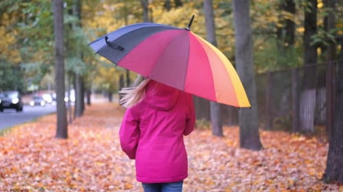 Petite fille riant jouant à la rotation avec un parapluie arc-en-ciel automne sur un érable orange doré tombé