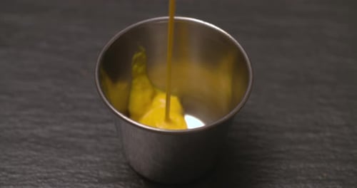 Pouring Yellow Mustard into a Small Steel Bowl