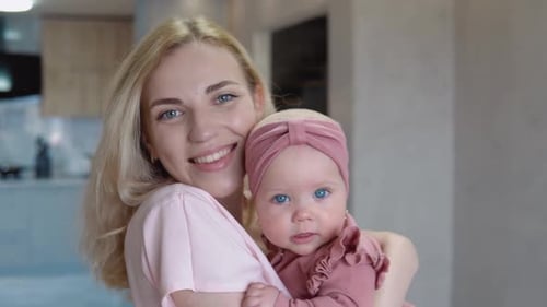 Mother and Baby Girl with Blue Eyes and Blond Hair Look at the Camera