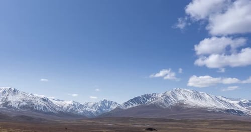 Timelapse of Sun Movement on Crystal Clear Sky with Clouds Over Snow Mountain Top. Yellow Grass at