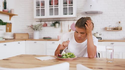 Frau sitzt am Tisch und sieht traurig aus und ist gelangweilt von Diät, die keinen Salat essen will