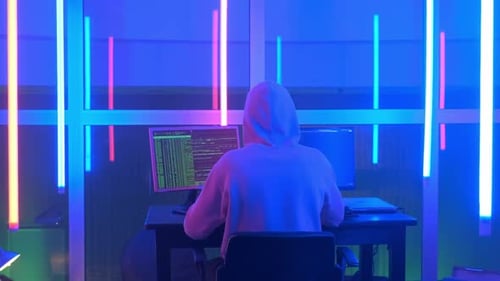Vue arrière à moyenne distance d'un hacker criminel travaillant le soir sur un ordinateur dans un grand bureau