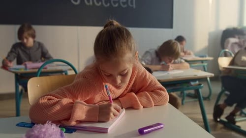 Young Students Writing at Desks in Classroom