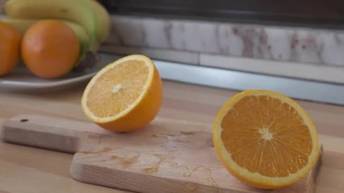 Orange fraîche coupée en deux se déplaçant latéralement d'avant en arrière sur une planche à découper en bois. - gros plan lent