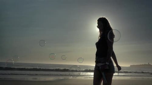 Young Woman Blowing Bubbles on a Beach at Sunset