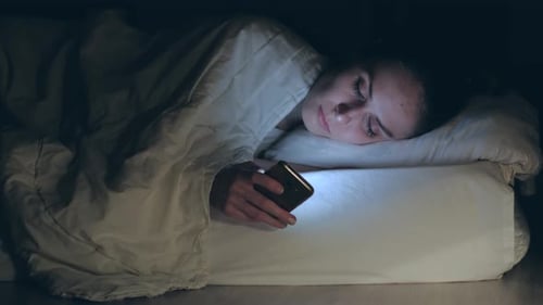 Woman lying in bed, falls asleep putting and turn off smartphone.