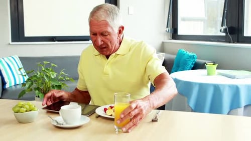 Senior Man Eating Breakfast While Using Tablet