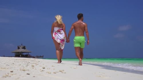 A couple walks on the beach holding hands at a tropical island resort hotel.
