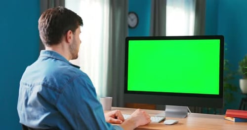 Closeup of a Man Uses Modern Computer with Green Mockup Screen While Sitting at the