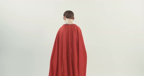 Boy with a superhero cape pretends to fly on a white studio background