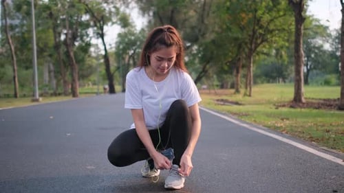Portrait of Asian sport woman sit and tight her shoelaces during exercise in green park