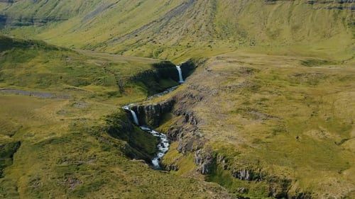 Drone Flight Over a Waterfall Descending in the Middle of the Green Hills in Iceland Summertime