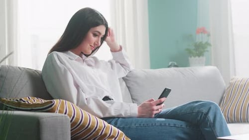 Woman Uses Phone While Relaxing on Couch