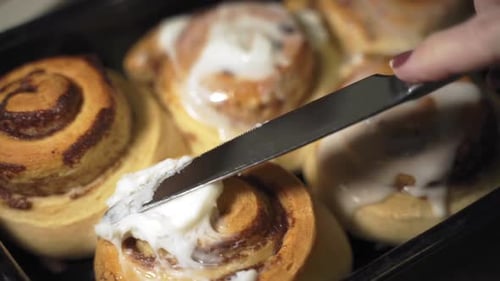 Slow motion close up knife spreading sweet icing on warm homemade cinnamon buns