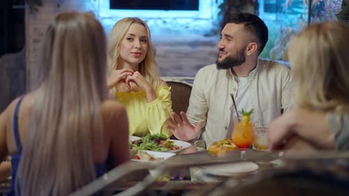 Cheerful Laughing Young Caucasian Couple Talking Sitting with Friends in Restaurant on Weekend