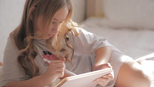 Young Woman Drawing on Tablet in Bed Sunlight