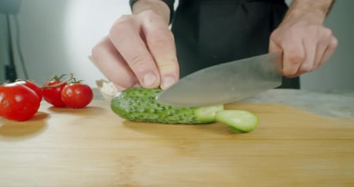 Chef Carefully Slicing Cucumber on Wooden Board