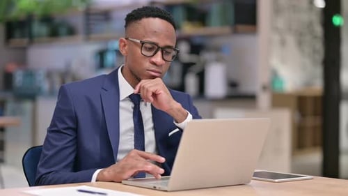 African Businessman Thinking and Working on Laptop in Office