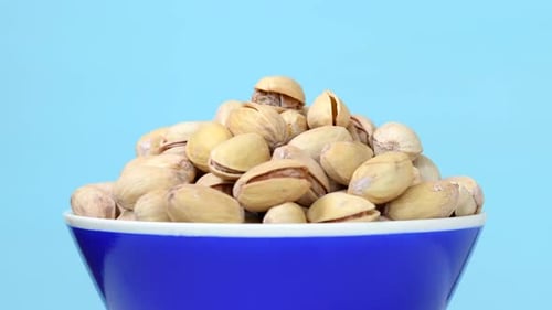 Roasted pistachios with salt in bowl rotating on blue background