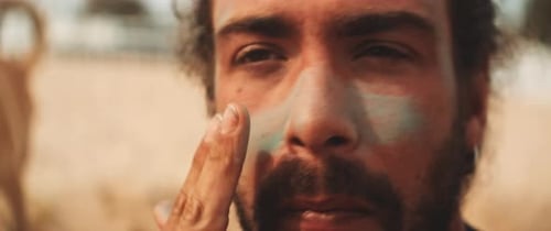 Young bearded surfer man applying green sunscreen on his face at the beach