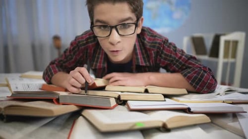 Junge studiert sorgfältig und aufmerksam Literatur, riesiger Bücherstapel auf dem Tisch