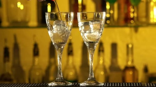 Pouring Clear Liquid Into Glasses with Ice Cubes