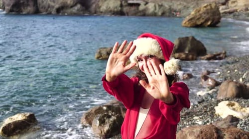Side View a Young Beautiful Sensual Woman in Santa Red Hat and Red Long Dress Posing on a Rock Above