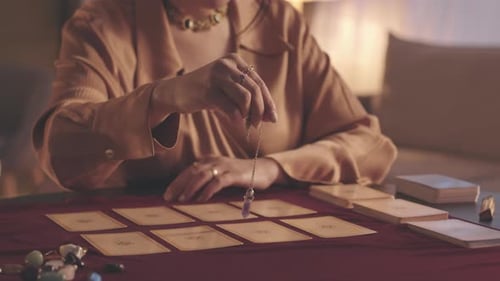 Hand of Fortune Teller with Pendulum over Tarot Cards