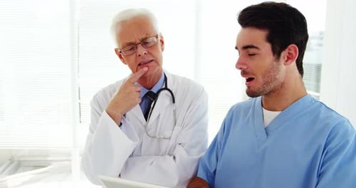 Male doctor and coworker discussing over digital tablet