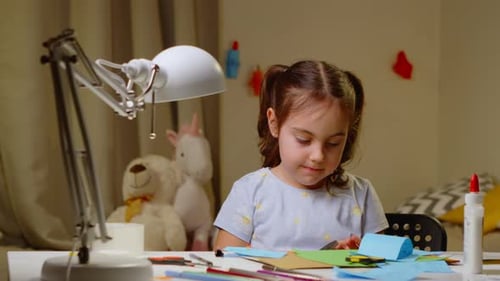 Preschool Girl Cuts Out Crafts From Colored Paper with Scissors
