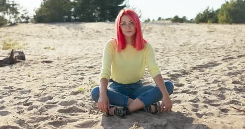 A Beautiful Smiling Girl is Sitting on Sand Outside on the Beach Pink Hair is Blown Away By the Wind