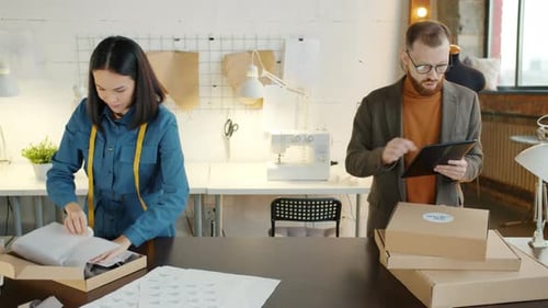 Tailoring Studio Employee Packing Clothes While Business Owner Checking Orders Using Tablet