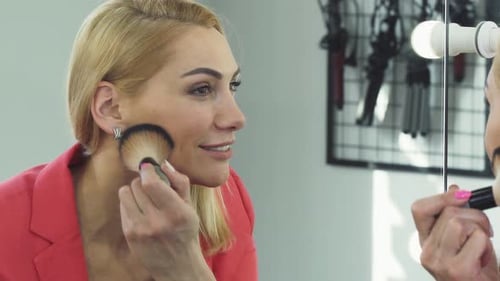 Woman Applies Makeup with Brush in Lighted Mirror