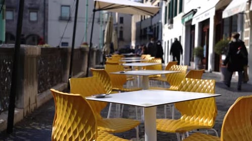 White Open Cafe Tables Stand Among Yellow Chairs on Sidewalk